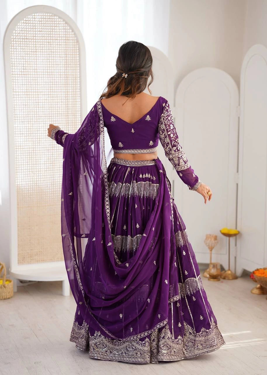Woman in a purple traditional outfit with silver patterns standing in a minimalistic room.